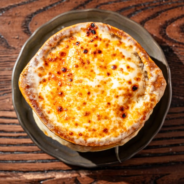 A close-up, top-down view of a bowl of French onion soup with melted, bubbly cheese.