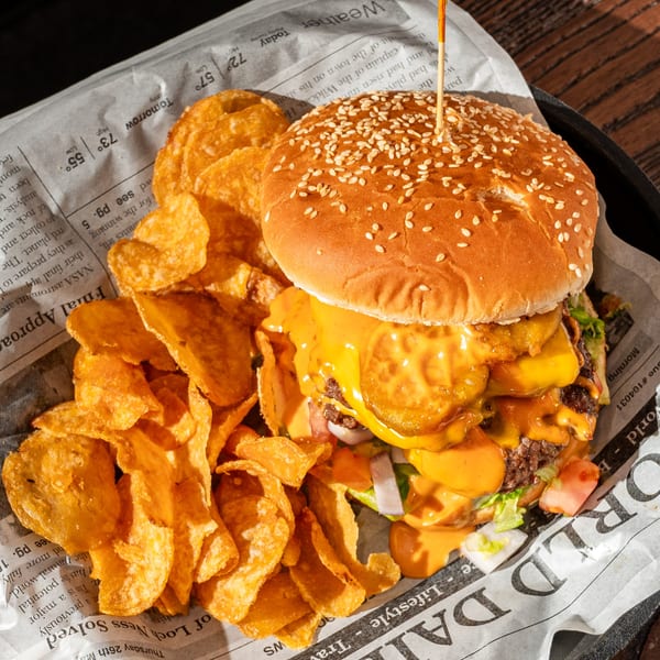 A juicy Eddington House double cheeseburger with melted cheese and chips on newspaper.