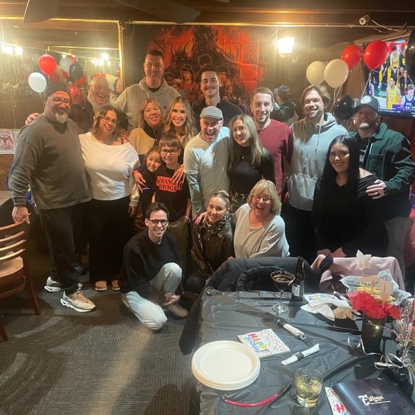 A large group of people celebrating a birthday at Eddington House, with balloons and a decorated table.
