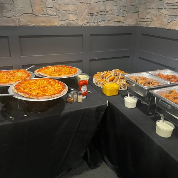 Buffet table with pizzas, cheesesteak sandwiches, chicken wings, and dipping sauces at Eddington House.