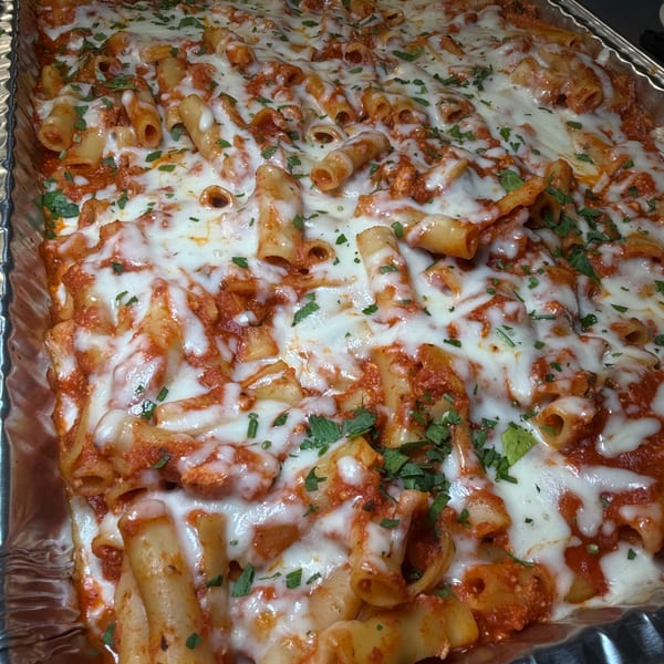 Baked ziti with melted mozzarella, rich red sauce, and fresh parsley in a foil pan.