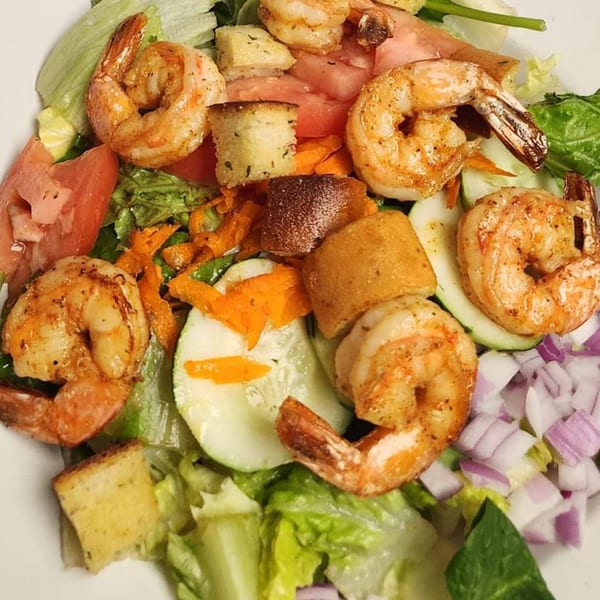 A vibrant shrimp salad with lettuce, tomatoes, cucumbers, red onions, and croutons.