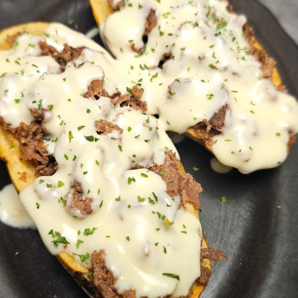 Two open-faced sandwiches with shredded beef, melted white cheese, and parsley on a dark plate.