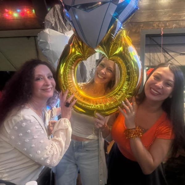 Three smiling women pose with a large gold and silver engagement ring balloon at Eddington House.